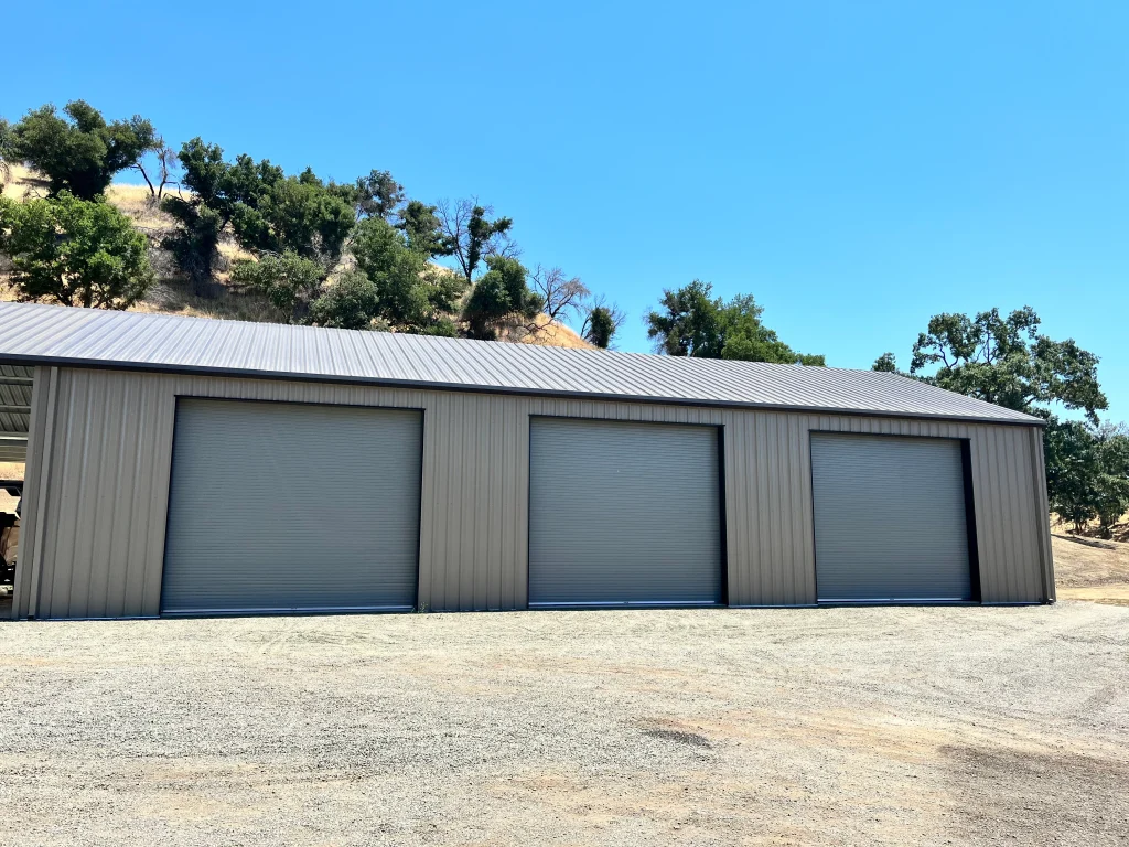 Three large grey metal roll-up Commercial Garage Doors installed on a modern industrial warehouse building.