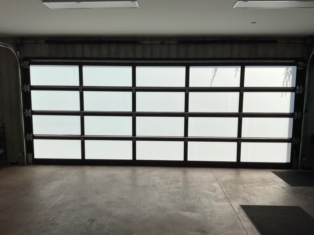 Interior view of a wide modern full-view glass garage door with a dark aluminum frame, offering guidance on How to Choose the Right Sectional Overhead Door for Your Home.