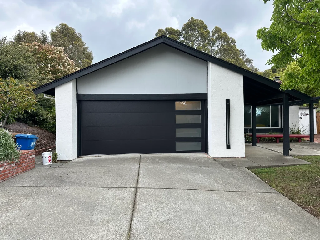 Modern dark grey garage door with vertical frosted window inserts installed on a contemporary home, illustrating factors that impact Sectional Overhead Door Cost.