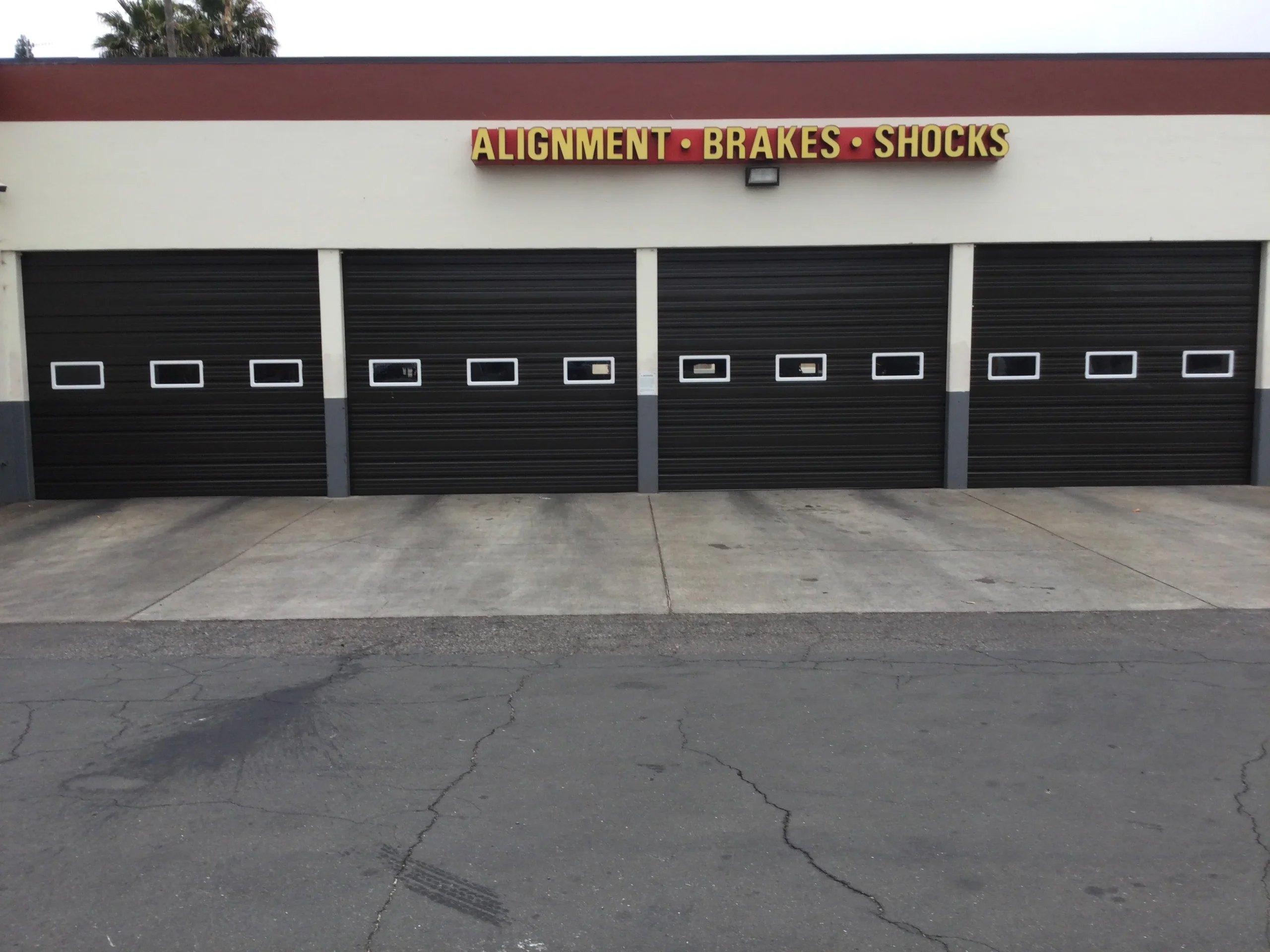 A line of dark commercial sectional bay doors with vision windows fronting an auto repair shop illustrating Why Businesses Choose Sectional Doors.