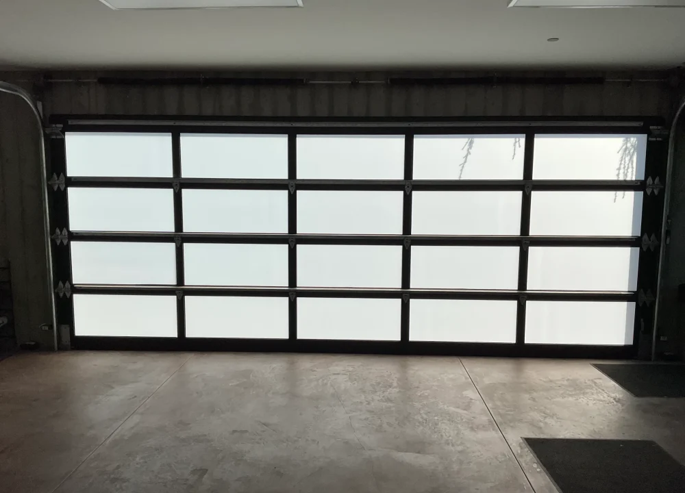 Interior view of a wide modern full-view glass garage door with a dark aluminum frame, offering guidance on How to Choose the Right Sectional Overhead Door for Your Home.
