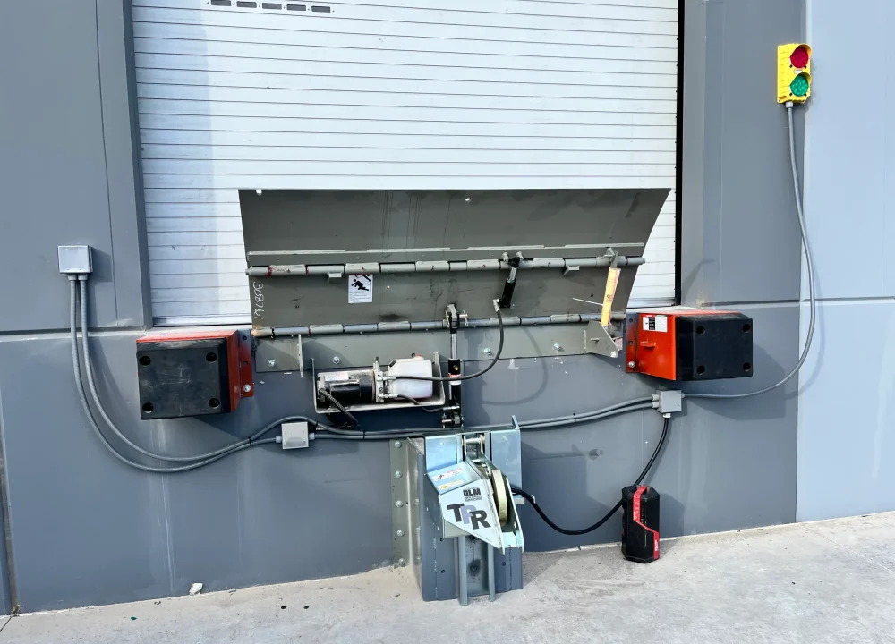 An exterior loading dock door equipped with a vehicle restraint lock, raised dock leveler plate, and signal light demonstrating Loading Dock Safety Rules.