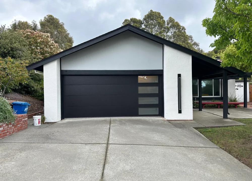 Modern dark grey garage door with vertical frosted window inserts installed on a contemporary home, illustrating factors that impact Sectional Overhead Door Cost.
